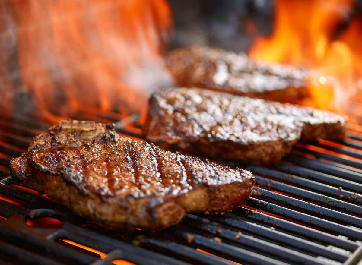 Picanha suculenta sendo fatiada sobre uma tábua de madeira ao lado de espetos e brasas incandescentes na churrasqueira