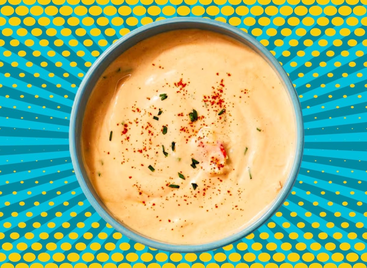 Uma mulher sorrindo enquanto segura uma caneca de sopa deli de frango, com uma folha de alface ao lado