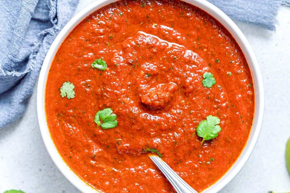 Taco recheado com molho ranchero, abacate, tomate e folhas de coentro ao lado de uma garrafa de água