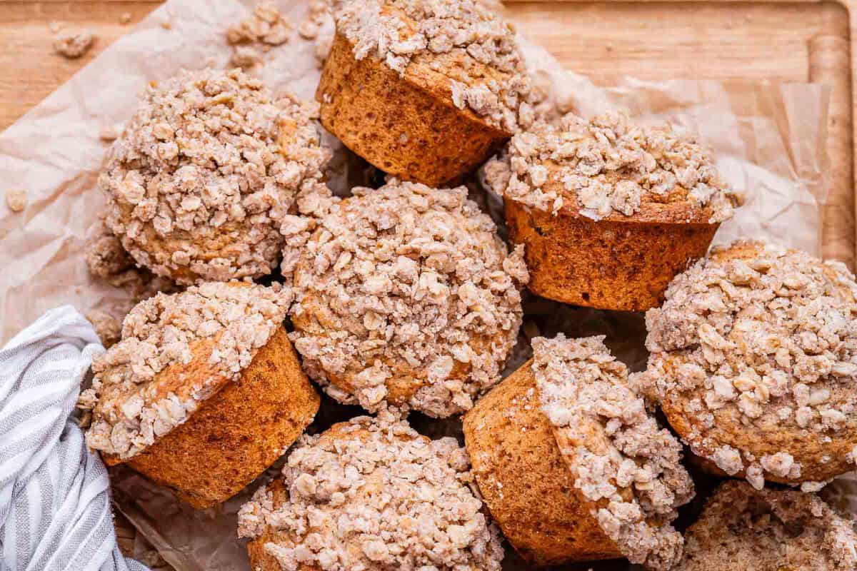 Muffins dourados de aveia e canela ao lado de iogurte grego, passas e um pote de canela em pó sobre uma tábua