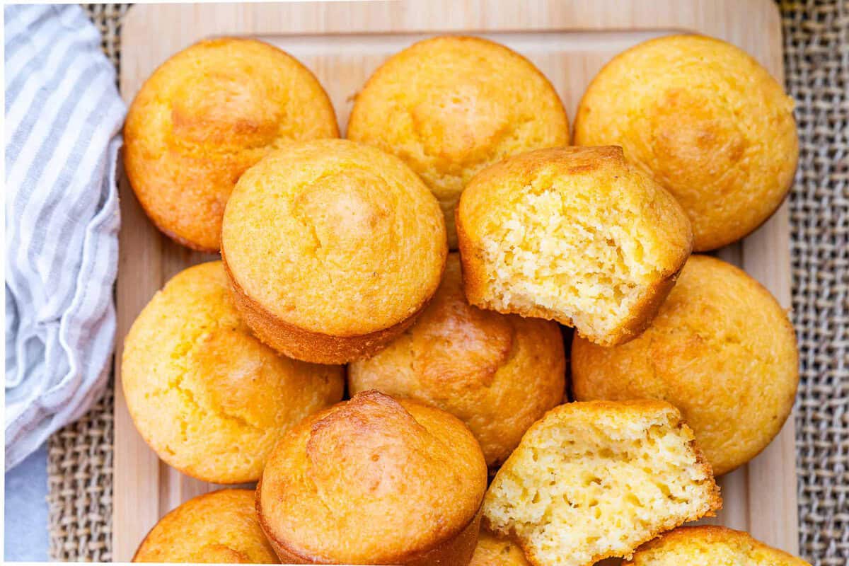 Muffins de milho dourados ao lado de iogurte grego, azeite e uma tigela de farinha, sobre mesa rústica