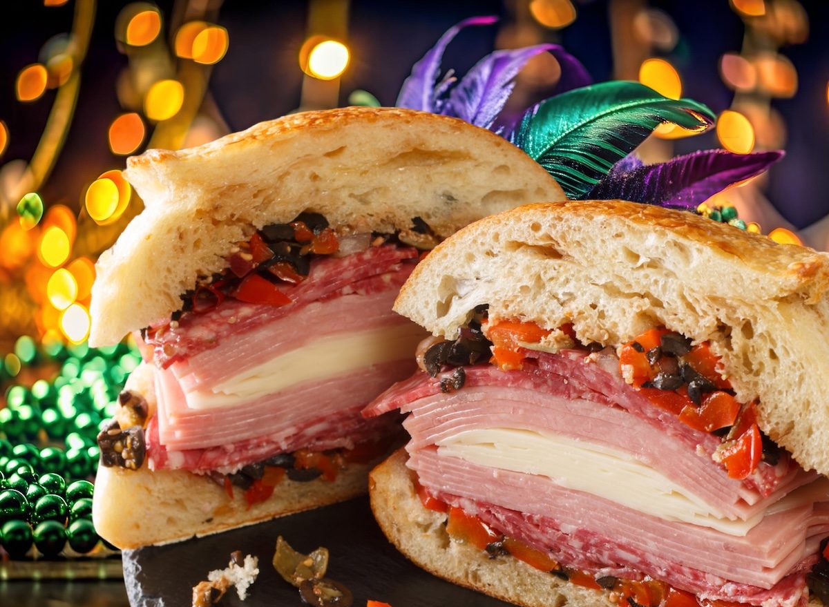 Muffuletta cortada ao meio, revelando provolone, carnes curadas, azeitonas e rúcula ao lado de garrafa de água