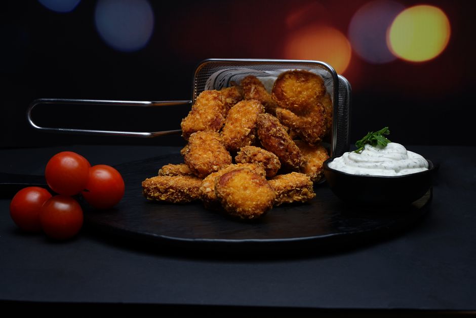 Mãos segurando nugget de frango crocante ao lado de uma balança e folhas de espinafre