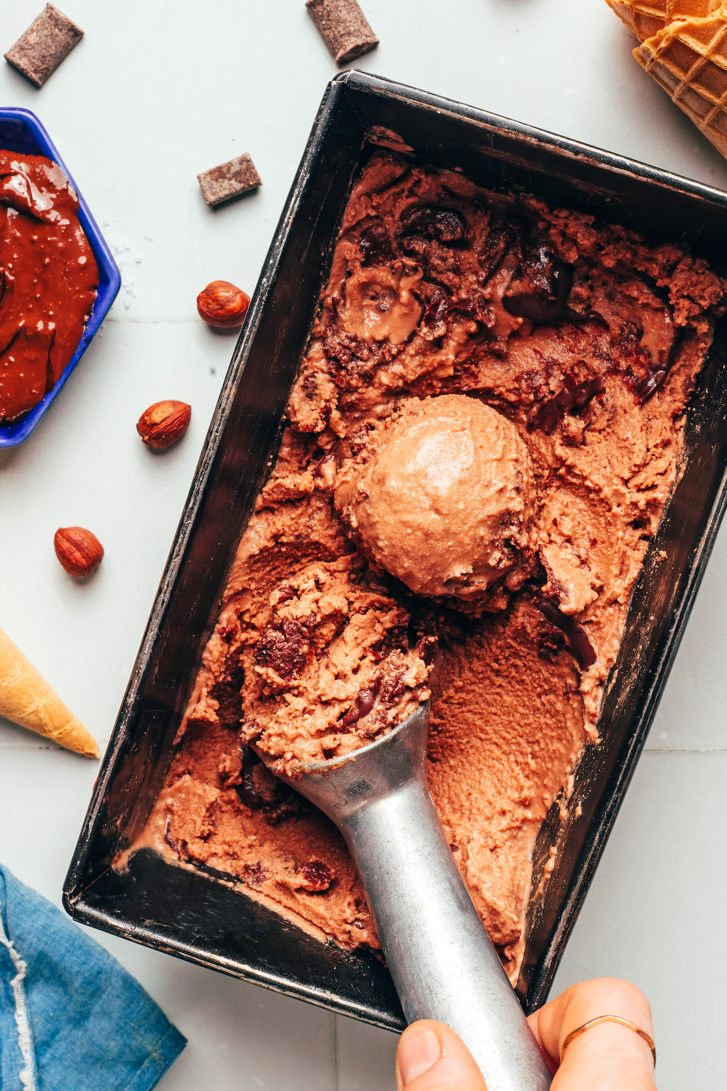 Uma pessoa segurando uma concha de sorvete vegano caseiro de Nutella com uma colher e uma garrafa de água ao fundo