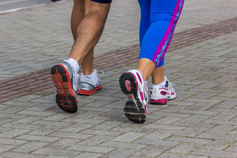 Pés descalços em uma praia arenosa, com um homem agachado em exercício de flexão do pé
