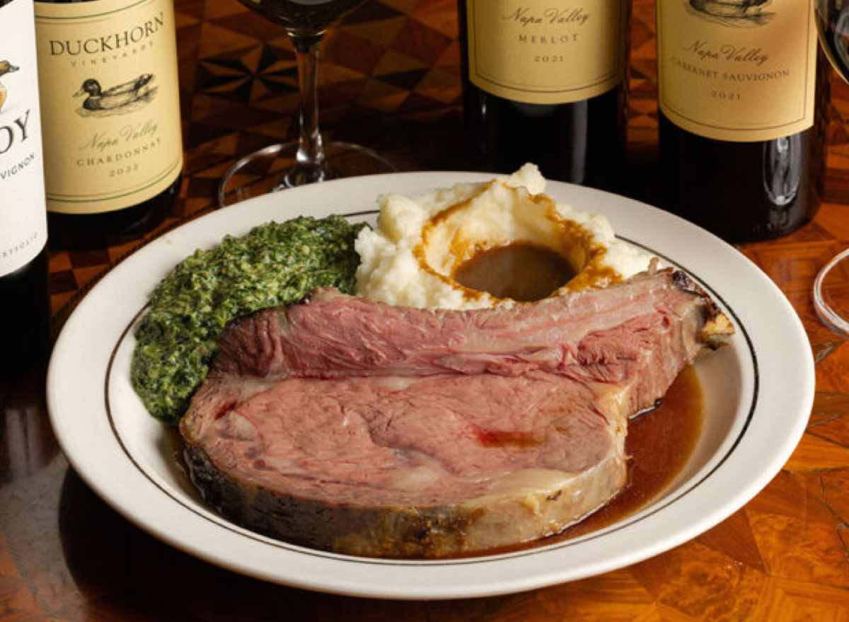 Prime rib suculento e fatiado em tábua de madeira, acompanhado de alecrim e taça de vinho tinto em ambiente elegante