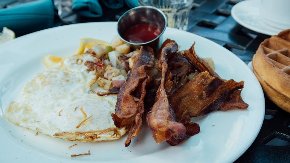 Prato com ovos fritos e fatias de bacon crocante dispostos sobre uma mesa de café da manhã bem iluminada