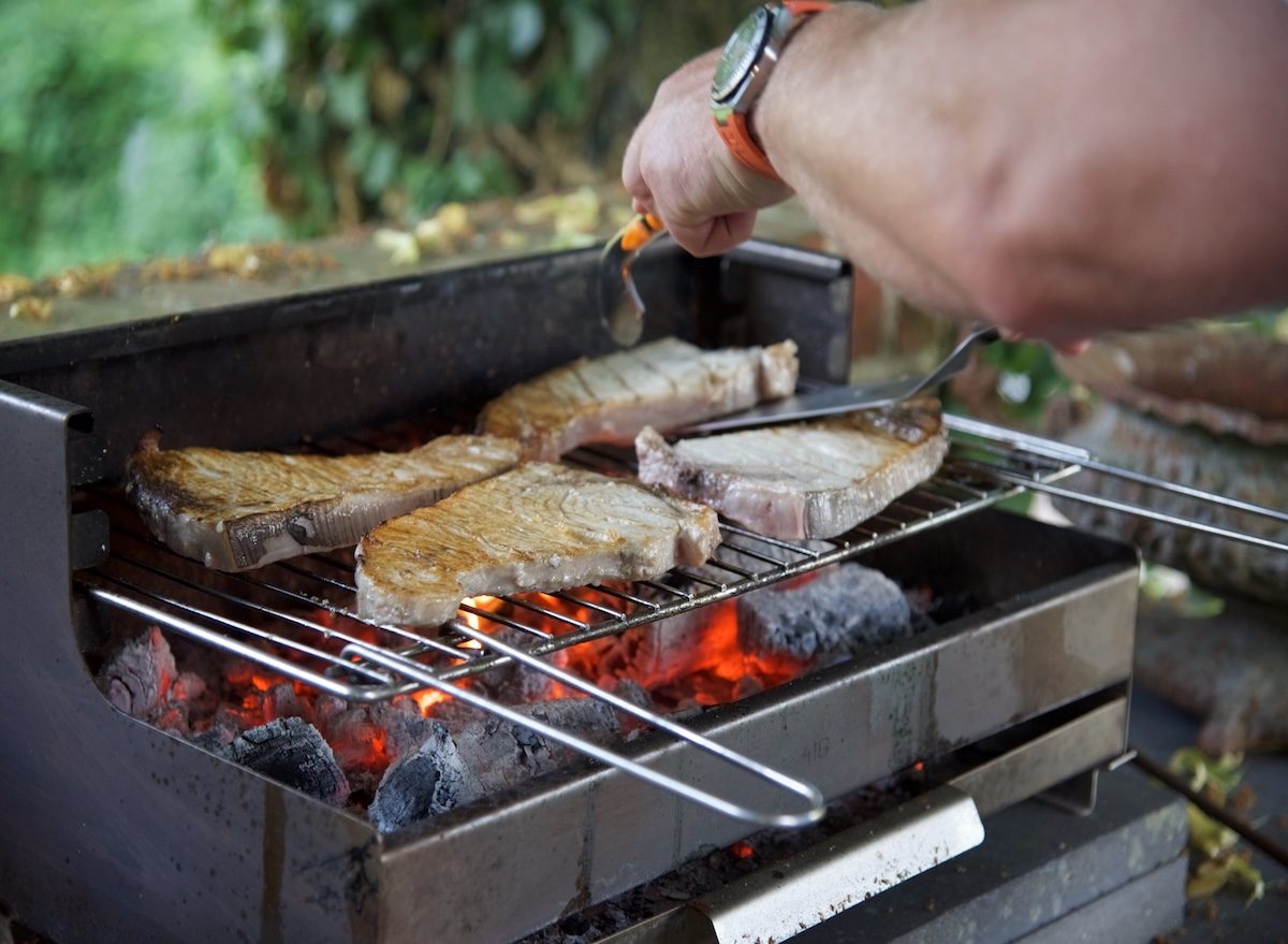Um pescado grelhado com fogo médio-alto, com tiras de limão e ervas frescas ao lado