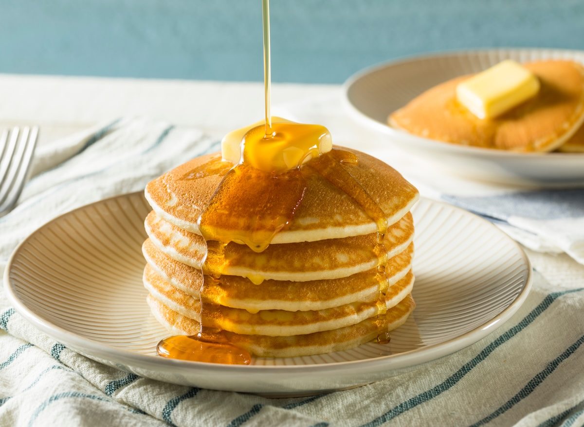 Panquecas fofas de buttermilk ao lado de whey protein, frutas vermelhas e um copo de água, sobre uma tábua de madeira