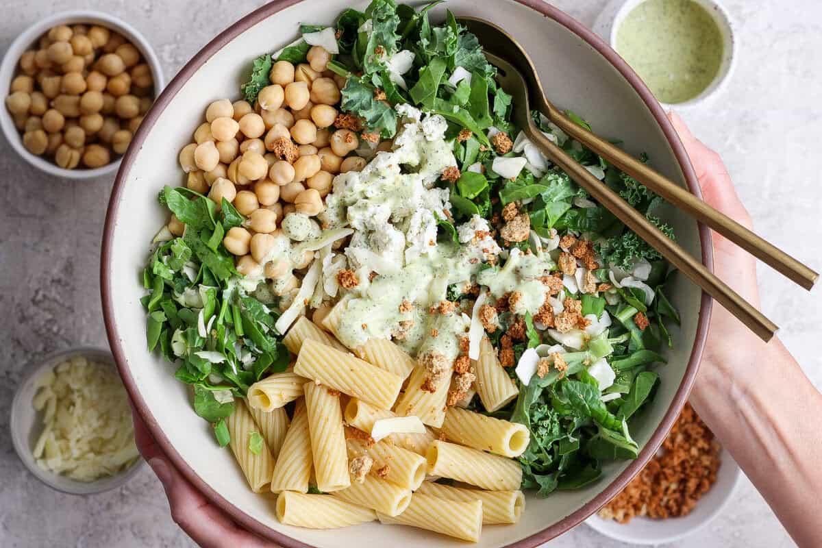 Uma tigela de rigatoni al dente coberta de molho verde, com espinafre, azeitonas, nozes e parmesão