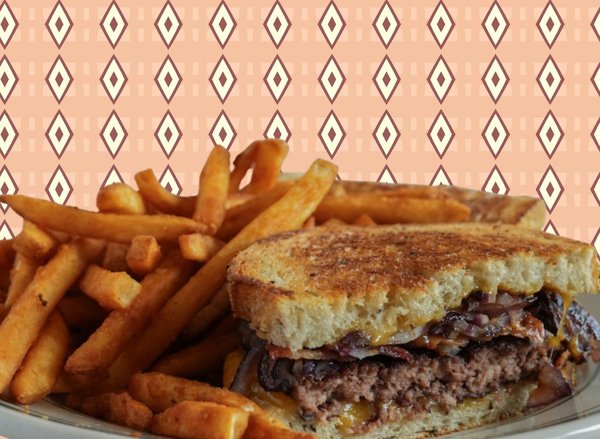 Patty melt dourado com queijo derretido, cebolas caramelizadas sobre pão integral, ao lado de folhas verdes