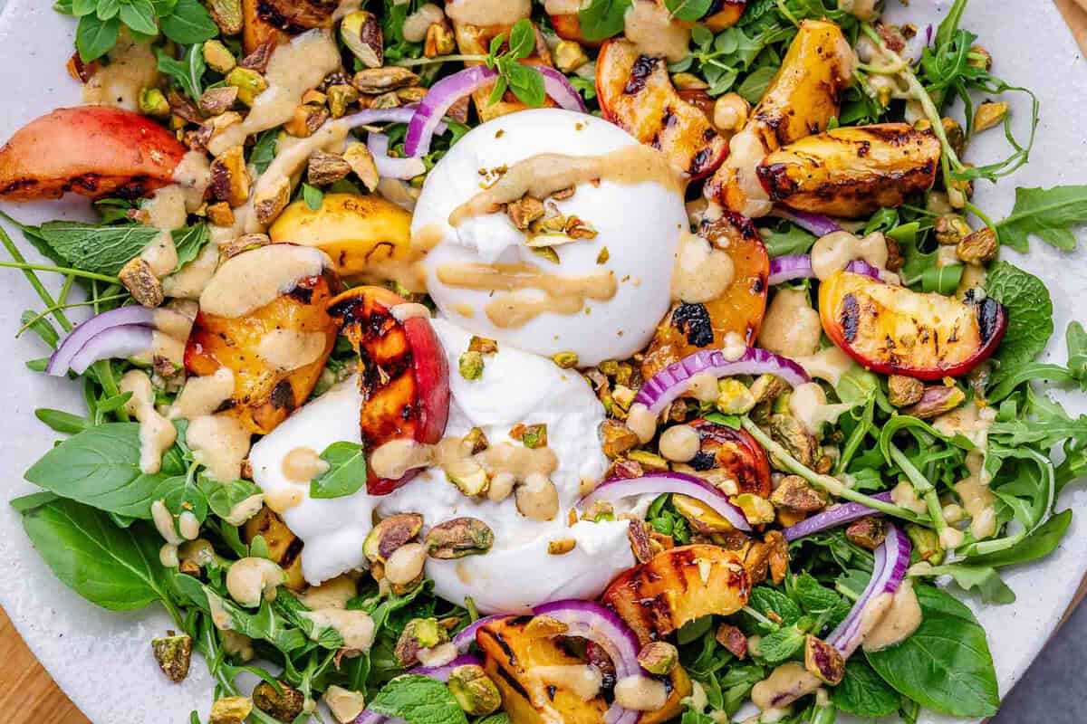 Burrata cremosa sobre cama de rúcula, rodelas de pêssego grelhado, melancia e fio de azeite