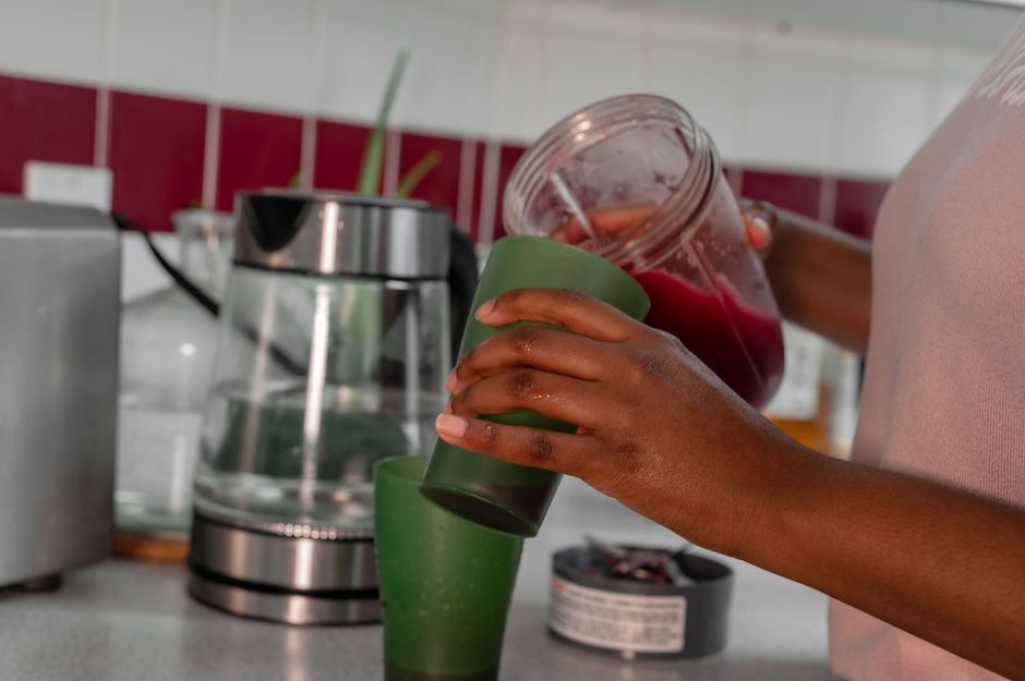 Liquidificador aberto exibindo banana fatiada, pote de pasta de amendoim, leite de amêndoas e iogurte grego