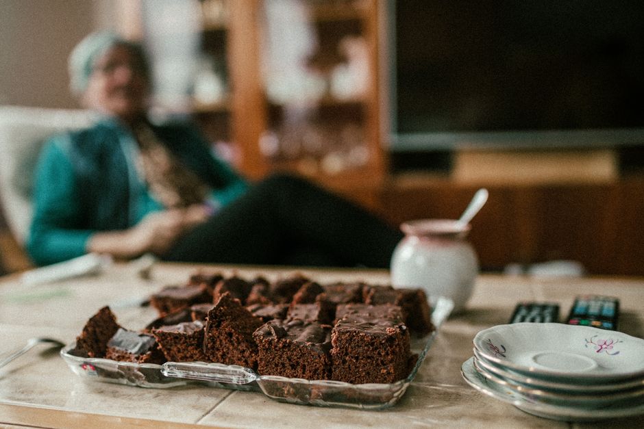Brownies de amendoim cortados, sobre papel manteiga, ao lado de potes de farinha de amêndoas e bananas maduras