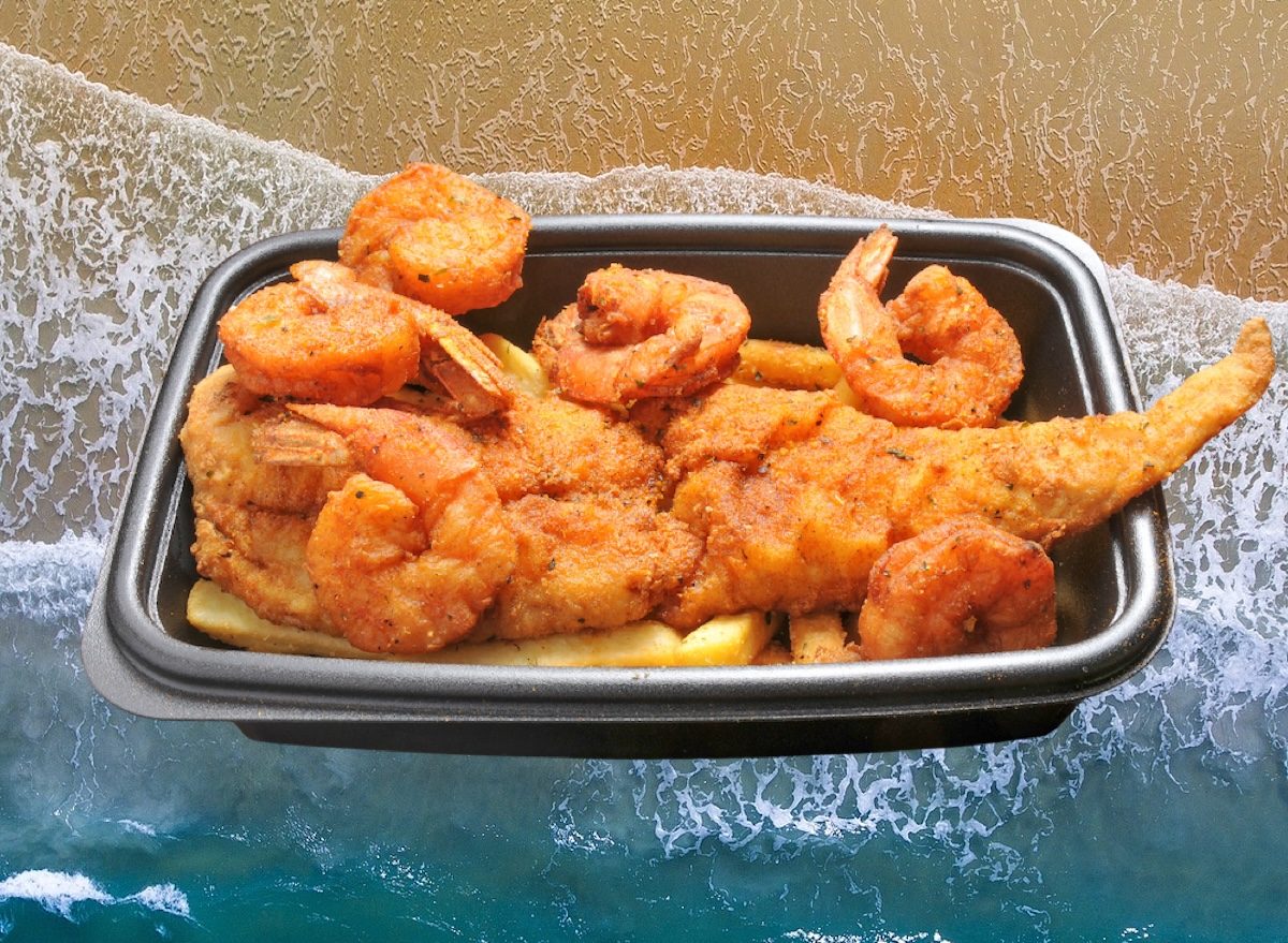 Filé de peixe dourado e camarões crocantes ao lado de limão, salsa fresca e folhas verdes numa travessa