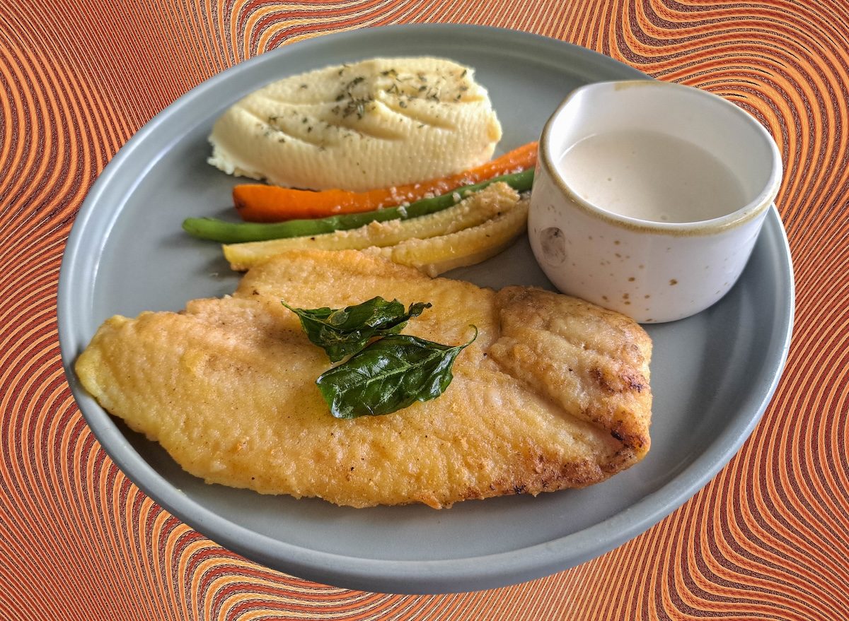 Prato com filé de peixe frito dourado ao lado de purê cremoso de batatas, acompanhado de limão e salsa