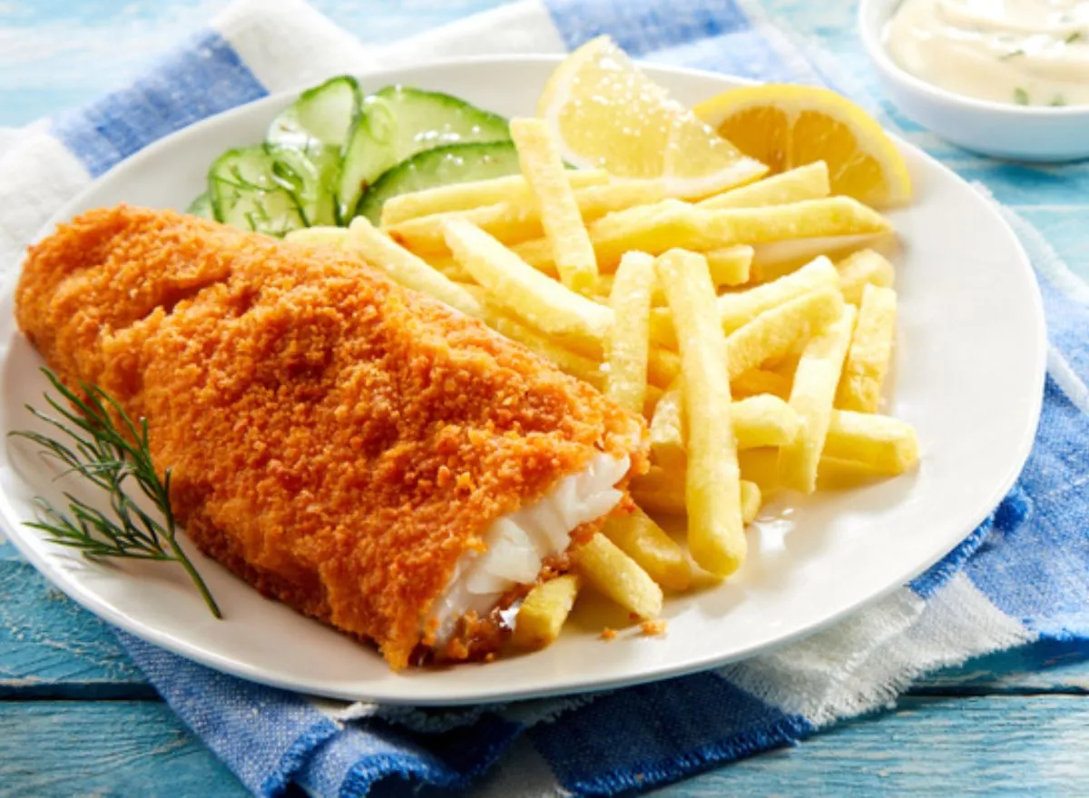 Peixe frito dourado em prato, ao lado de limão, folhas de rúcula e uma garrafa de água mineral