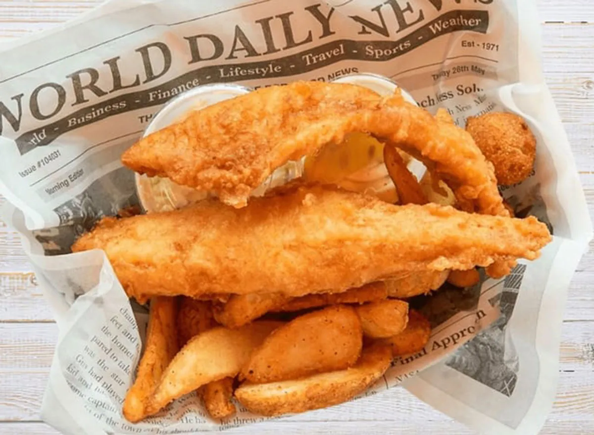 Filé de peixe dourado na airfryer ao lado de rodelas de limão e uma salada fresca em prato de cerâmica