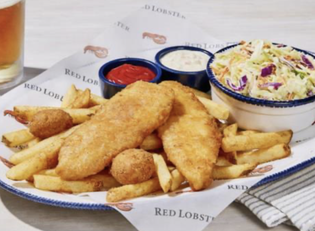 Um peixe frito crocante sobre uma tábua de madeira, com hush puppies ao lado e um copo de refrigerante