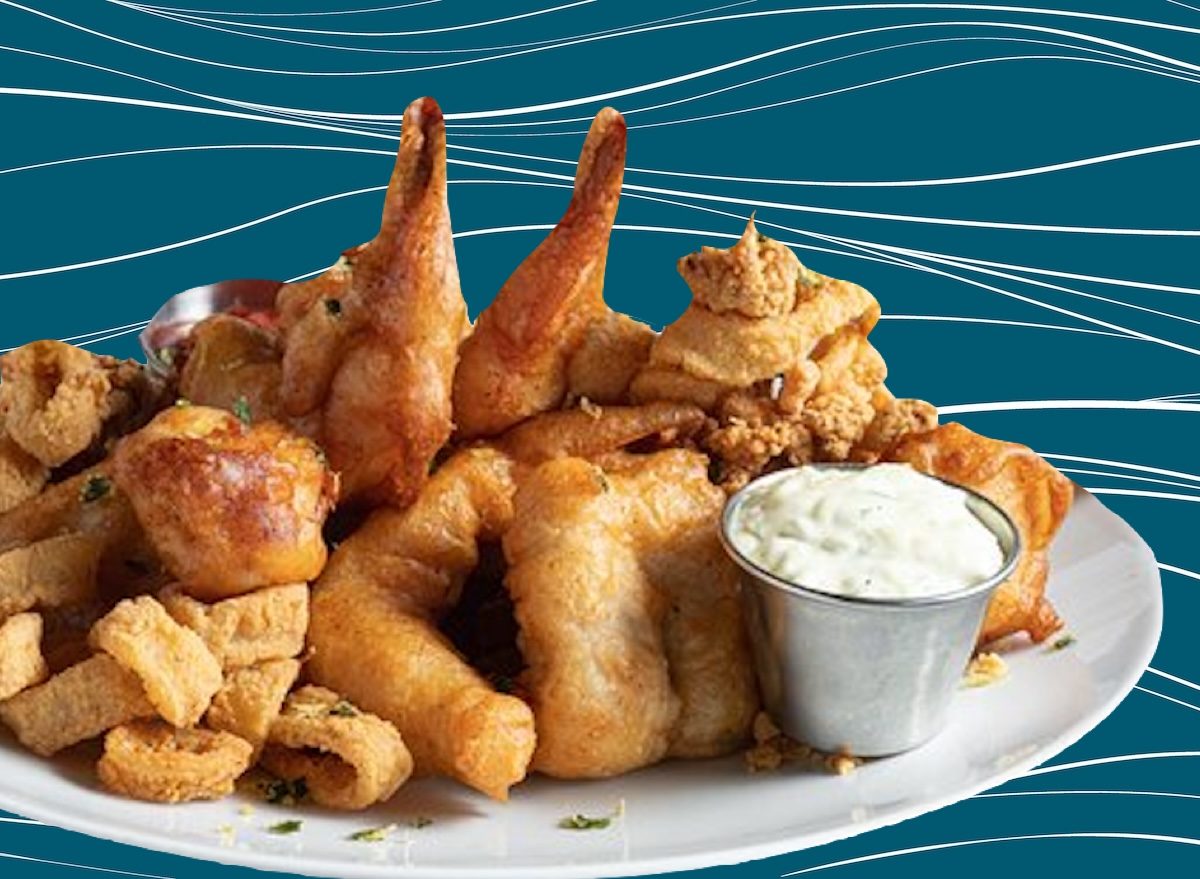 Um peixe frito crocante em uma assadeira de prata, com fatias de limão e folhas de alface ao redor