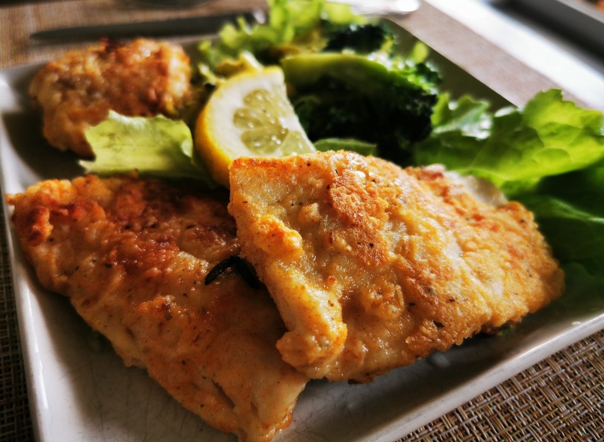 Um peixe frito crocante, com camada dourada e acompanhado de vegetais frescos
