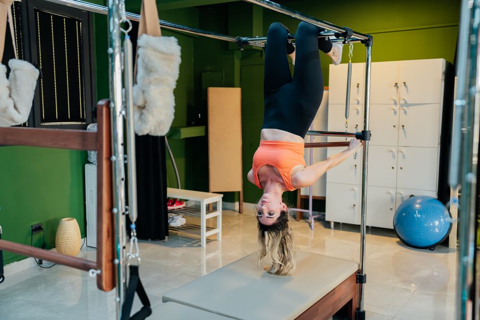 Pessoa em roupa esportiva executa o “roll‑up” de Pilates sobre colchonete, segurando uma faixa elástica e mantendo postura alinhada