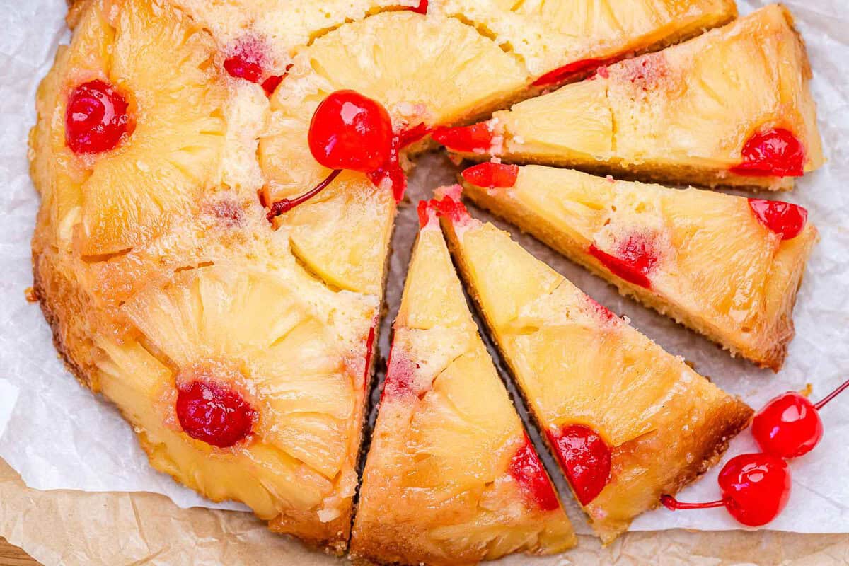 Fatias de Pineapple Upside-Down Cake sobre prato branco, ao lado de abacaxi fresco, iogurte grego e colher de mel