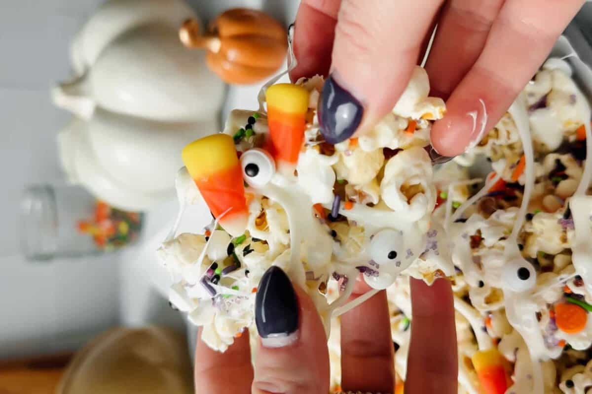 Pipoca dourada em tigela de vidro, coberta por tiras brancas de marshmallow, candy corn laranja e confeitos coloridos