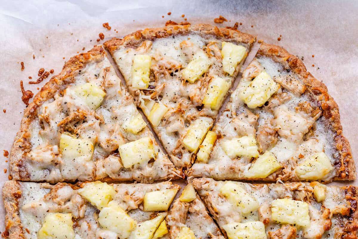 Uma pessoa sorrindo enquanto corta uma pizza com base integral e recheada com vegetais no fogão