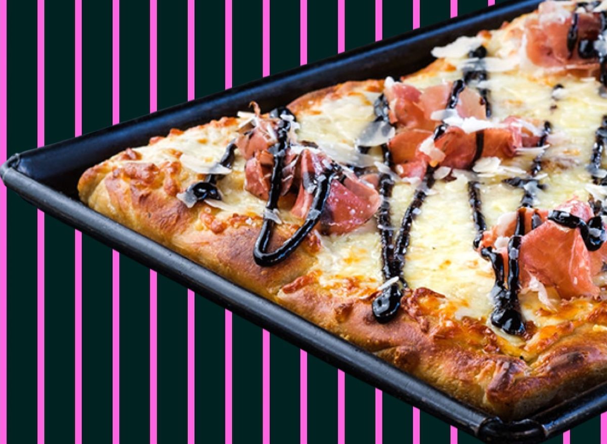 Um atleta segurando fatia de pizza siciliana ao lado de salada verde e garrafa de água