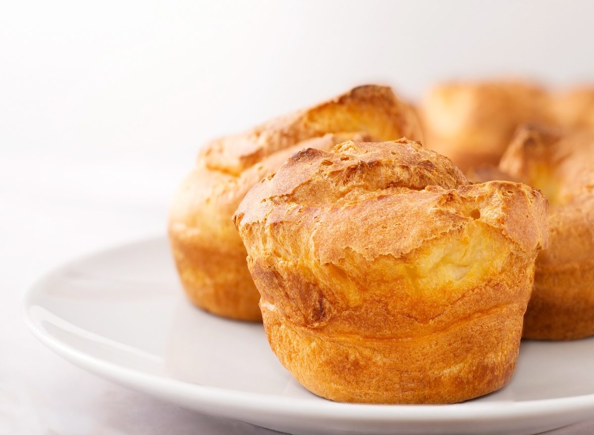 Popover dourado ao lado de iogurte, frutas vermelhas e água, sobre bancada clara