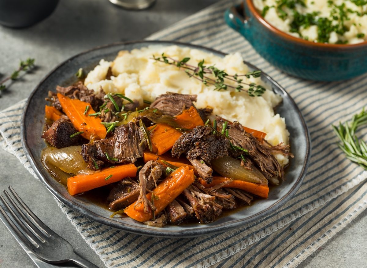 Prato com pot roast suculento ao lado de purê de batata cremoso coberto por queijo ralado, bacon crocante e salsinha