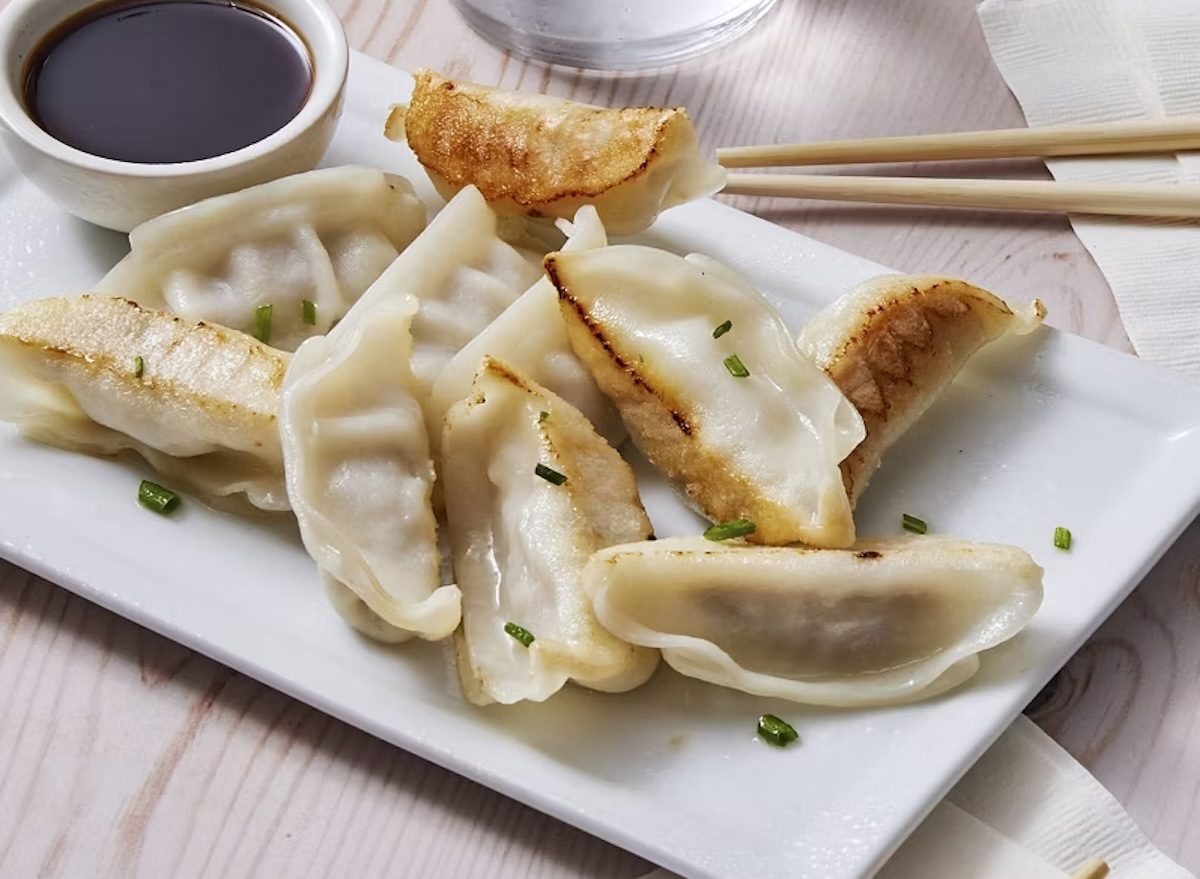 Uma pessoa comendo potstickers congelados em uma mesa com frutas frescas e um copo de água