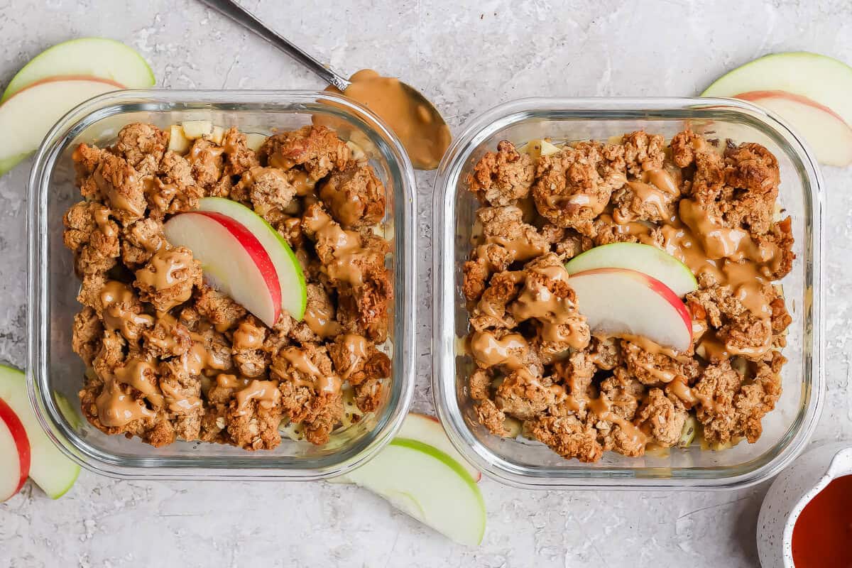 Tigela de apple crisp dourado com aveia, colher de proteína do soro e fatias de maçã sobre tábua de madeira