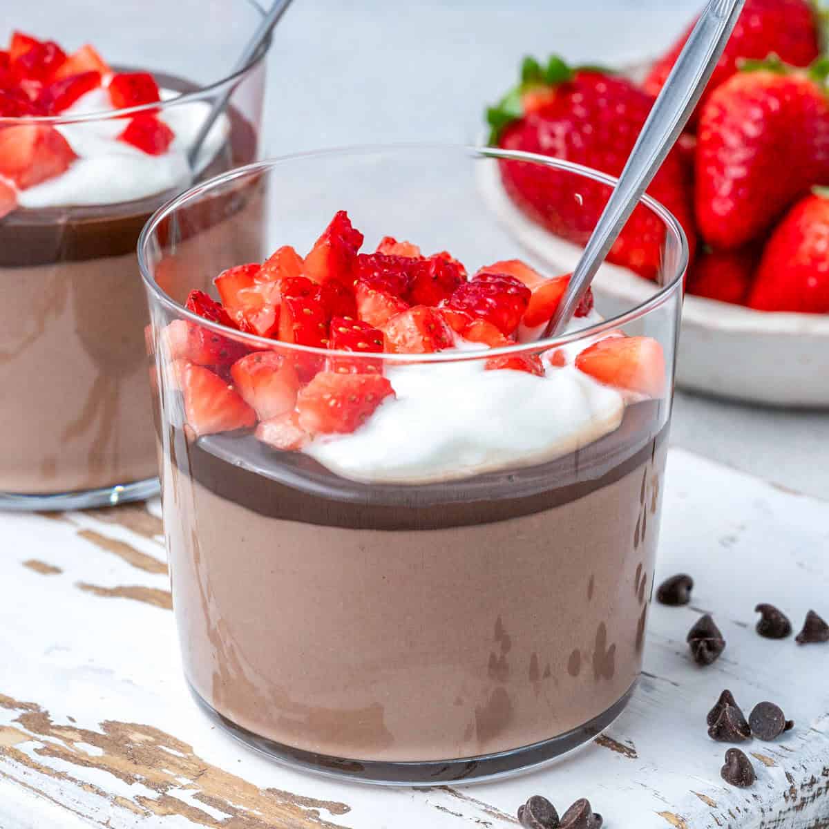 Pudim de chocolate cremoso em uma taça, decorado com raspas de cacau e ao lado de um pote de queijo cottage fresco