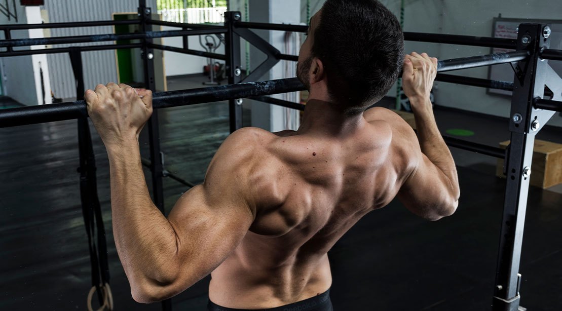 Uma pessoa realizando um pull-up com uma mão apoiada em uma barra de treino, enquanto o outro braço segura um peso de treinamento