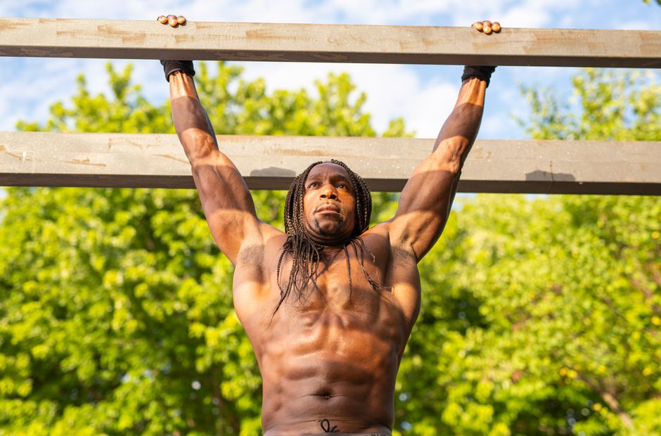 Mulher com braços estendidos, fazendo um pull-up, com uma barra de treino em segundo plano