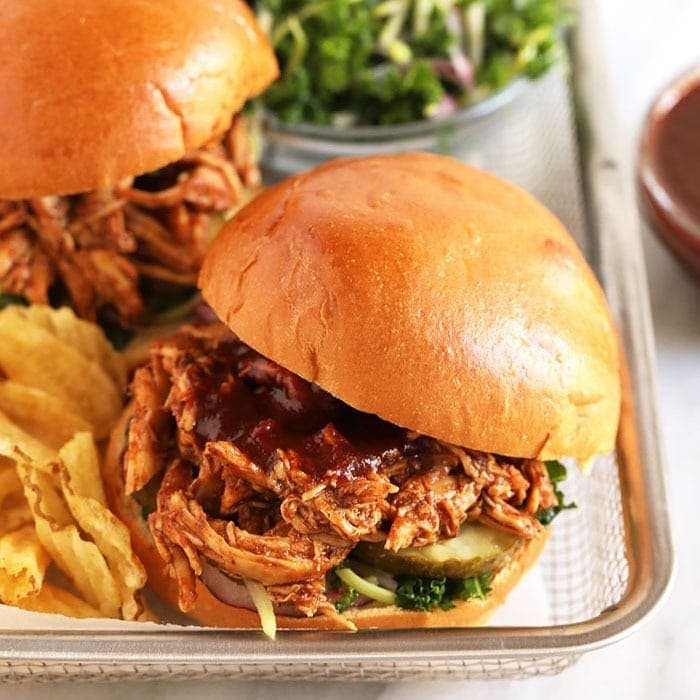 Um frango cozido em uma slow cooker com molho bbq, acompanhado de vegetais frescos e uma colher de sopa de alho picado