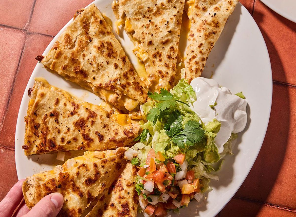 Uma tortilla crocante ao lado de um prato com queijo derretido e recheio fresco de vegetais