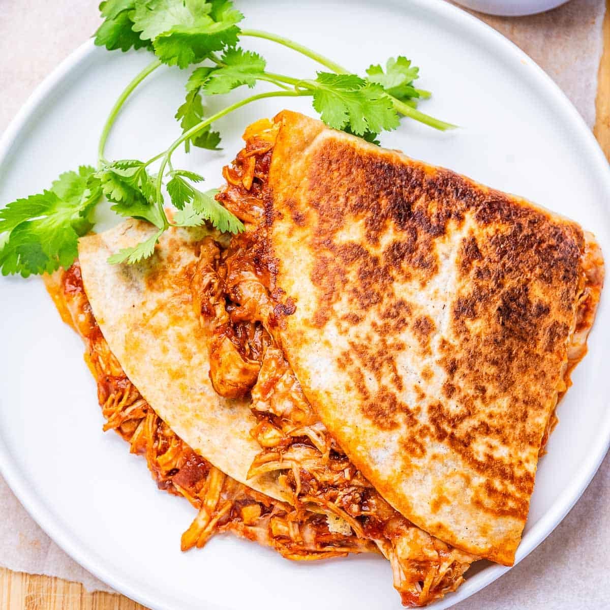 Uma quesadilla aberta com frango desfiado, molho de chipotle e queijo derretido em cima de uma tábua de madeira