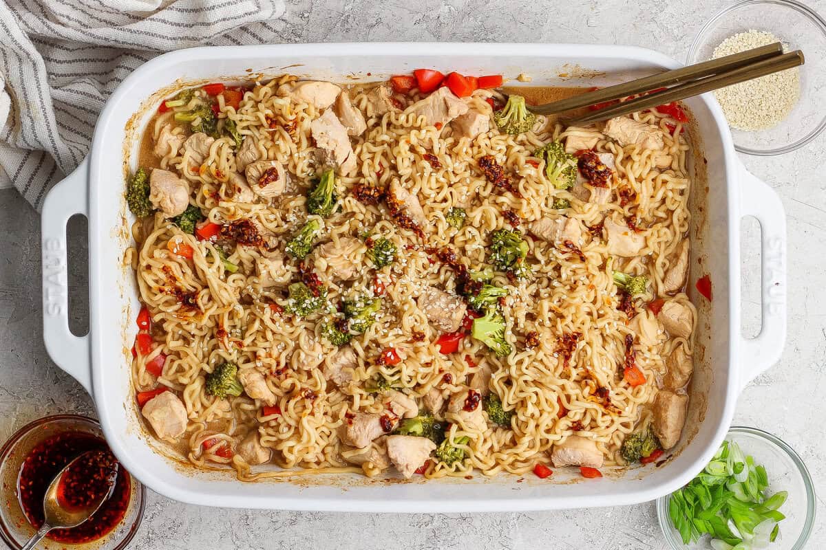 Tigela de ramen assado com vegetais frescos e proteína, disposta sobre uma mesa de madeira com temperos ao lado
