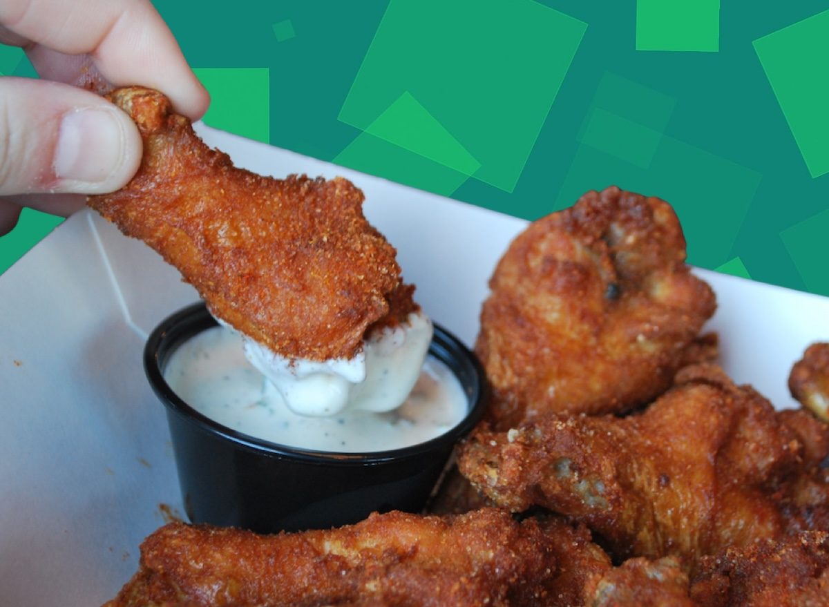 Um copo de ranch dressing cremoso com folhas de alface e pepino em segundo plano
