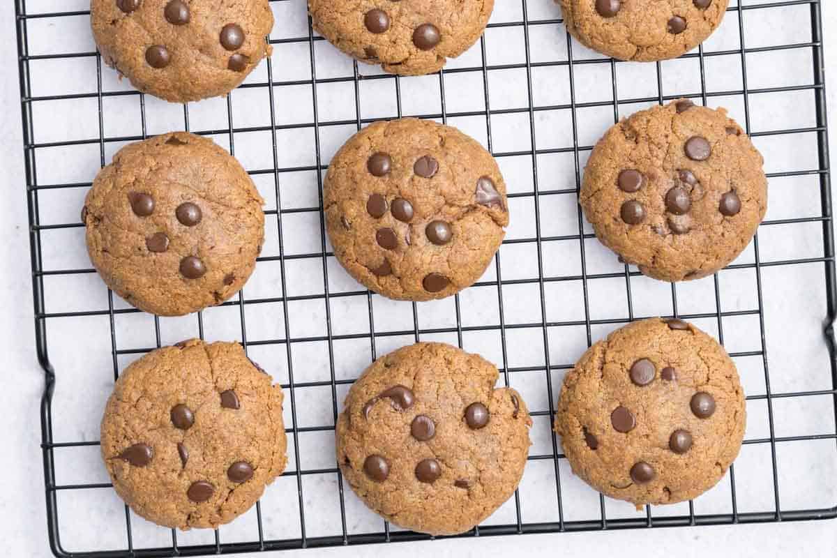 Pote de whey protein ao lado de cookies caseiros, amêndoas e uma balança de precisão sobre uma mesa de madeira