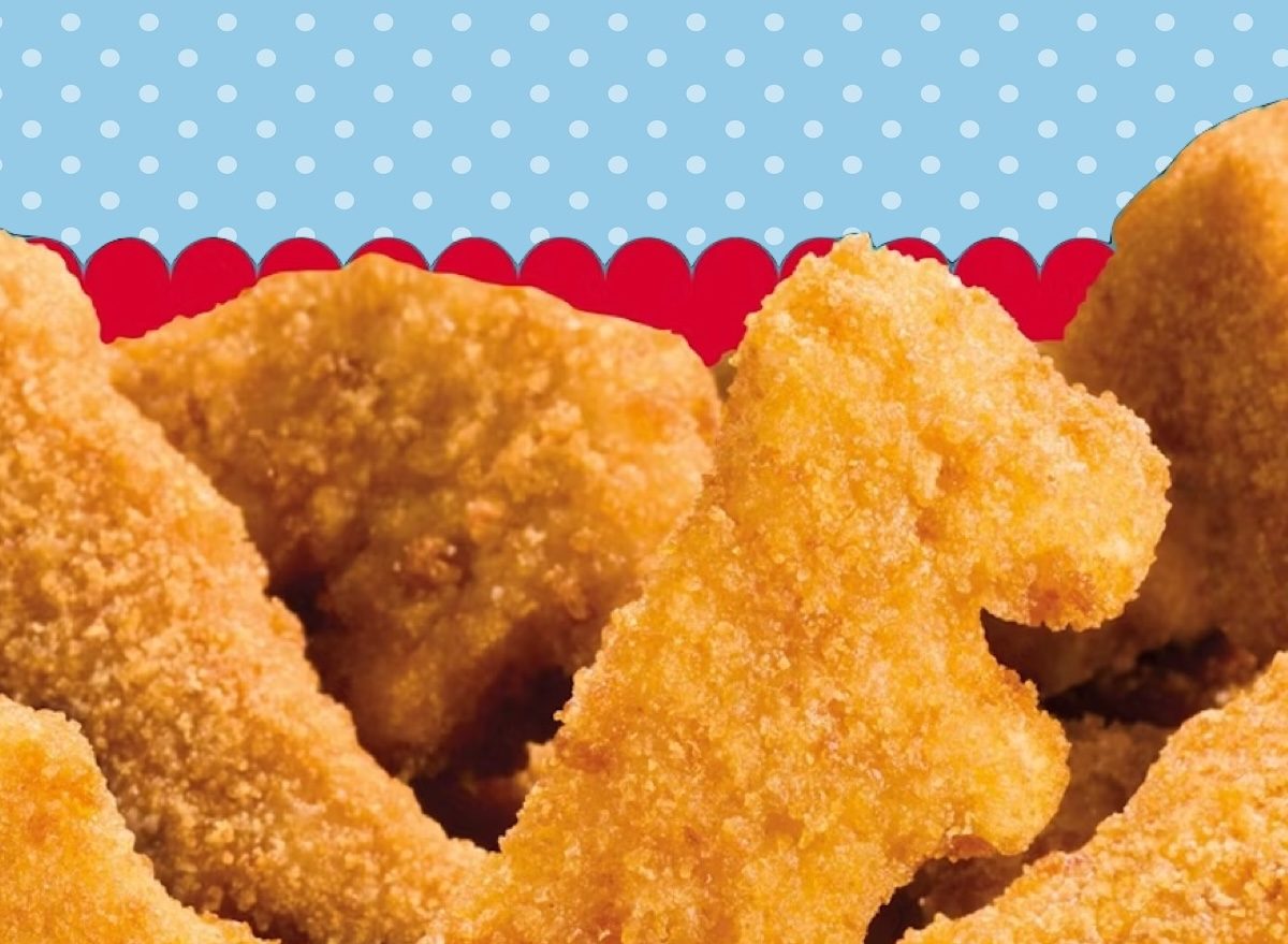 Uma criança sorrindo enquanto segura uma porção de nuggets congelados, com um prato de macarrão ao lado