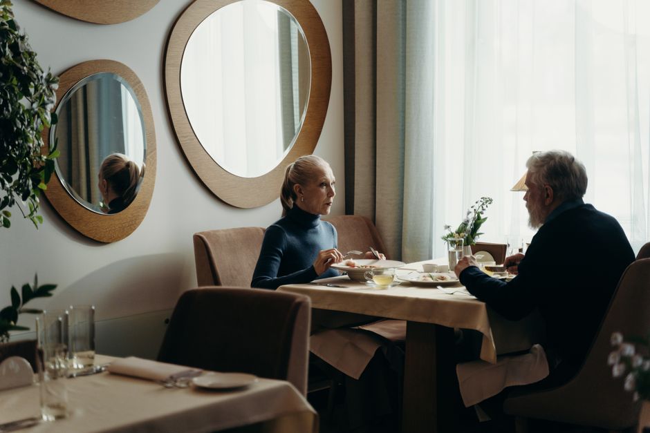 Casal de 60 anos sorrindo enquanto saboreia salada colorida e suco natural em restaurante com placa de desconto