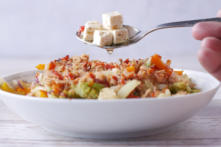 Tofu esfarelado em uma tigela rústica com ervas frescas, azeite e colher de servir sobre uma mesa de madeira clara