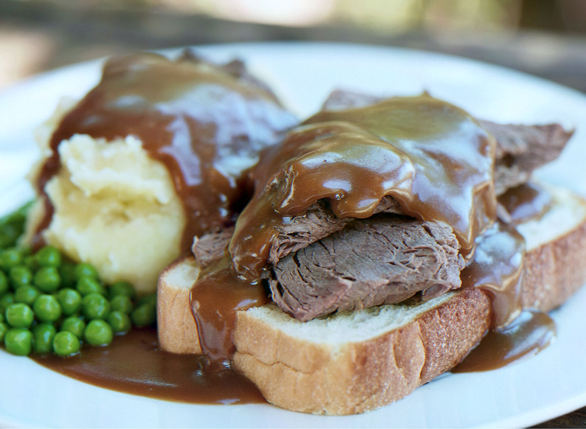 Um pedaço de roast beef assado, cortado fino, com um corte de alcatra, servido aberto sobre uma folha de alface