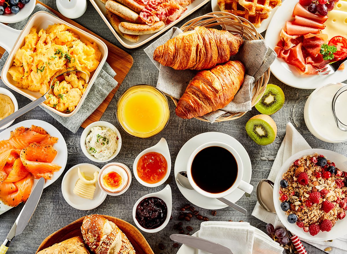 Buffet de café da manhã com frutas frescas, pães variados, ovos mexidos, iogurte, granola e copos de suco natural
