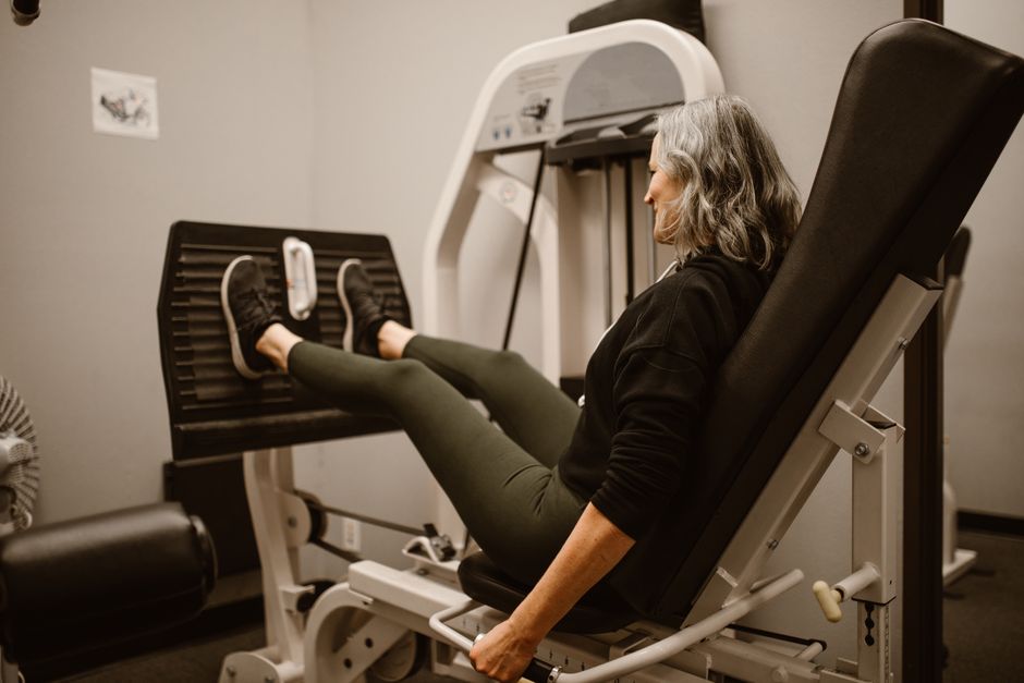 Uma pessoa sentada em uma cadeira, com as pernas estendidas para frente e as mãos apoiadas na parte inferior da cadeira
