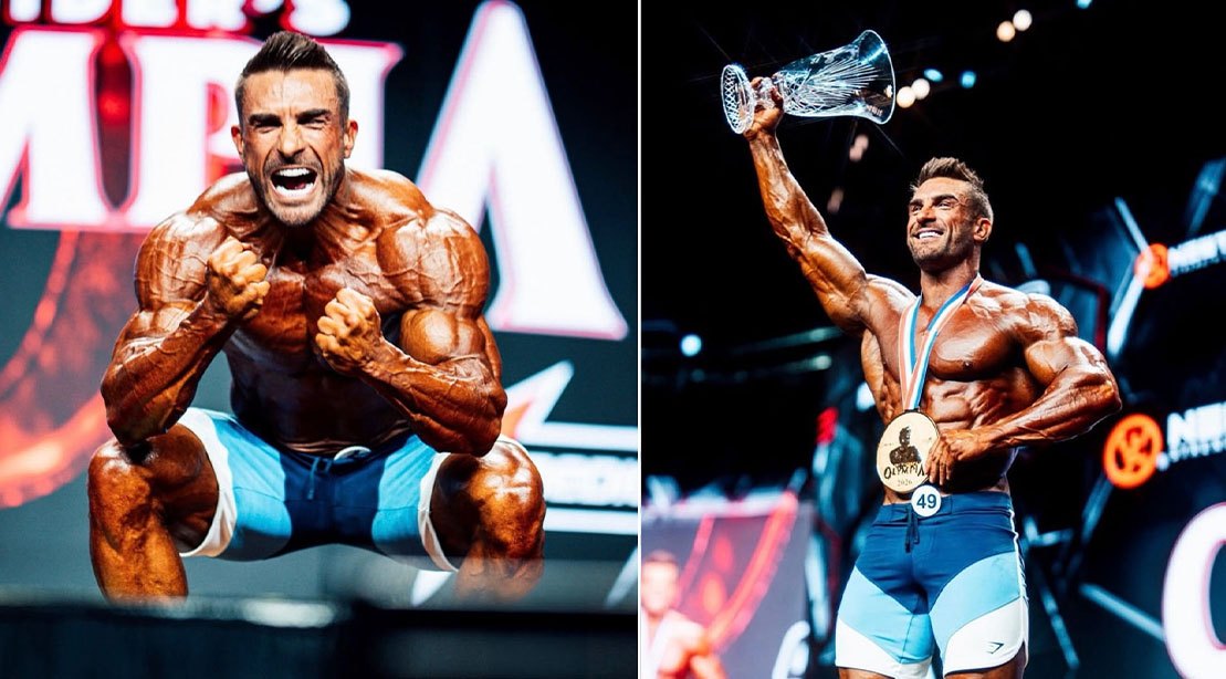 Ryan Terry levanta o troféu no palco, exibindo músculos definidos, enquanto usa cinta lombar e luvas de treino